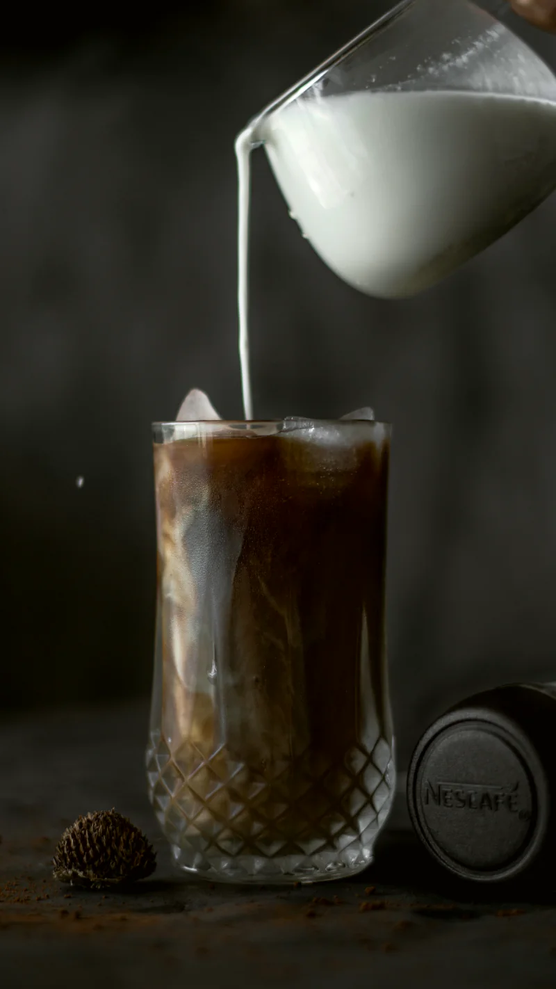 Cold milk poured into a tall glass of iced coffee.