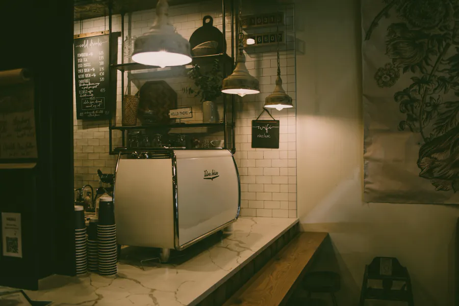 A café counter with an espresso machine under pendant lamps.