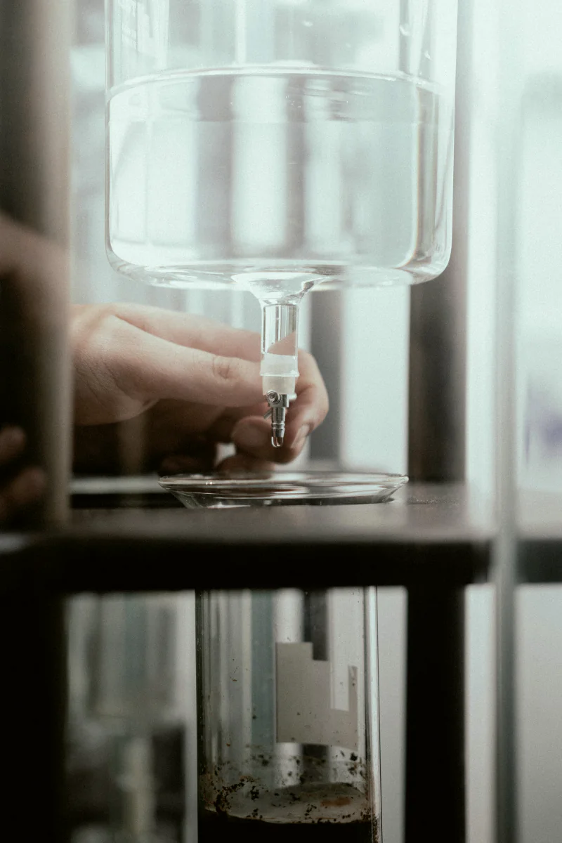 A hand adjusting a glass cold-drip coffee tower.