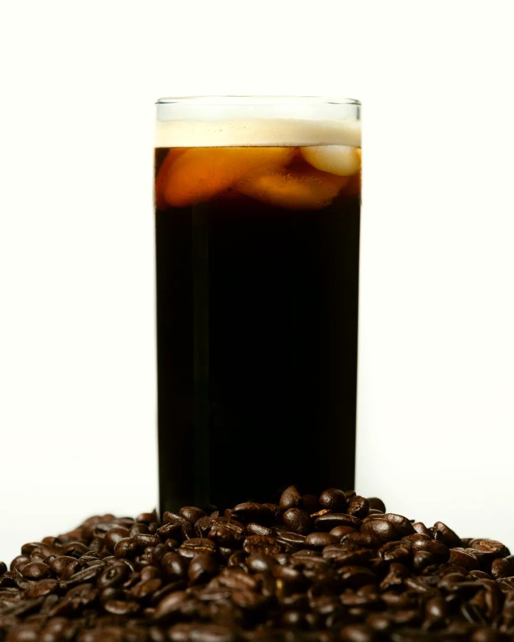 A tall glass of cold brew standing in roasted coffee beans.
