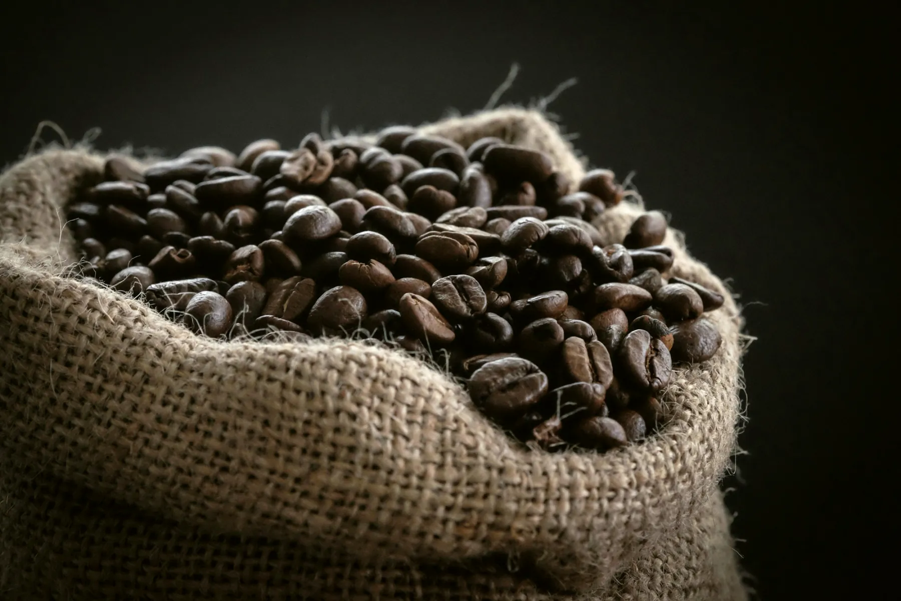Freshly roasted coffee beans spilling from an open burlap sack.